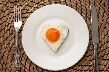 Çırpılmış yumurta, beyaz bir tabakta kalp şeklinde. Cihazların yanında jüt peçetenin üstünde.