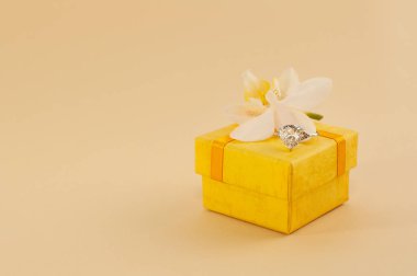 Sarı bir kutunun üzerinde büyük bir değerli taş ve bej arkaplanda orkide olan bir yüzük.