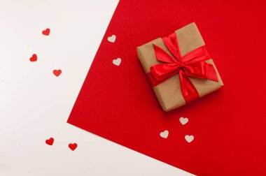 El işi paketlerinde hediye kutusu ve kırmızı beyaz arka planda kalpleri olan kırmızı bir kurdele.