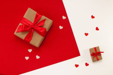 El işi paketlerinde hediye kutuları ve kırmızı beyaz arka planda kalplerle kırmızı kurdeleler.