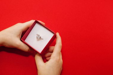 Çocukların elleri kırmızı zemin üzerinde büyük bir mücevher olan yüzüklü bir kutuyu tutuyor.