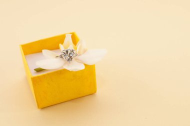Orkide çiçekli sarı hediye kutusu ve bej arka planda büyük değerli taşlı bir yüzük.