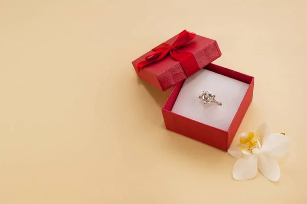 蘭の花の隣にある赤いギフトボックスに大きな宝石のついた指輪 — ストック写真
