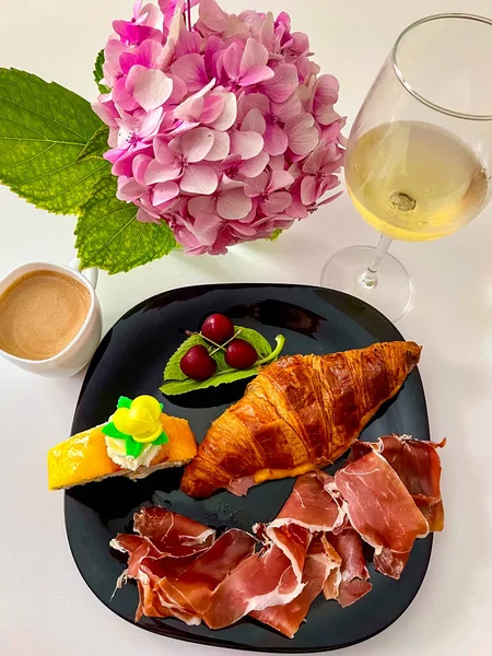 Bir fincan kahve, kruvasan, şarap, jambon, çiçekler, dikey fotoğraf.