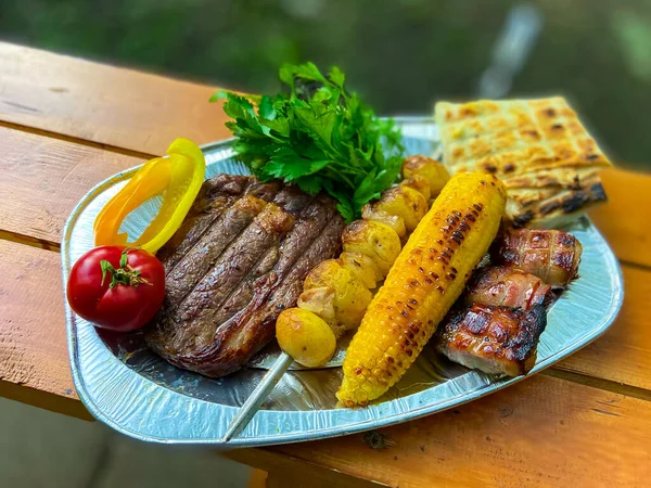 Izgara biftek, patates, mısır, tabakta sebze.