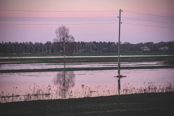 electric pole in flood water in Latvia  in early spring, purple dramatic sky