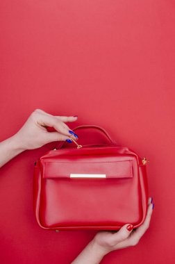 Parlak yaz moda aksesuarları. Kırmızı arka planda kırmızı deri çanta ya da el çantası. Parlak manikür torbalı kadın elleri. Üst Manzara. Düz Yat.