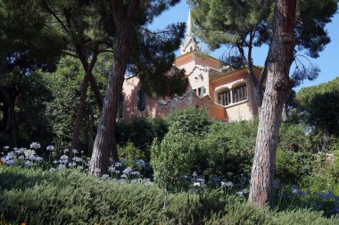 İspanya, Barselona - Temmuz 01.2019 Gaudi 'nin Guell Park' taki evi güneşli bir havada ağaçların arasında.