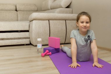 Gülümseyen küçük kız spor yapıyor, yoga yapıyor, evde spor yapıyor. Yoga minderinde yatıyor, kollarına dayanıyor..