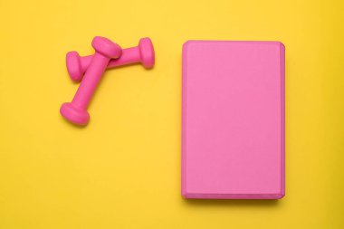 Sarı arka planda iki fuşya çiçeği ve yoga bloğu. Metin için yer