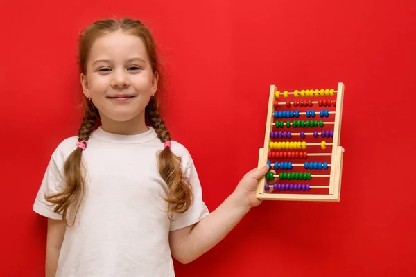 Happy little girl holds abacus in hands. On red background. Royalty Free Stock Photos