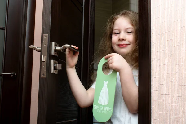 Little girl with painted lipstick peeks out from behind a door that says Dress to impress Dont Disturb — Stockfoto