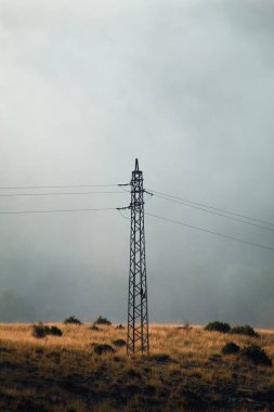 Arka planda güzel bir sabah sisi olan yüksek voltajlı çelik bir direk..