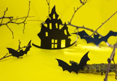 Cadılar Bayramı ve dekorasyon konsepti - yarasalar, balkabakları, kasvetli kağıt ev, sarı arka planda kara ağaç dalları. Katlanmış kağıttan yapılan Origami sanatı. Kesik yarasalar ve diğer dekorasyonlarla Cadılar Bayramı arka planı.
