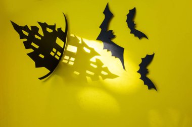 Cadılar Bayramı - yarasalar, balkabakları, kasvetli kağıt ev, sarı arka planda kasvetli siyah ağaç dalları. Evden bir gölge, cadılar bayramının kasvetli gölgeleri ile kağıttan yapılmış bir ev.