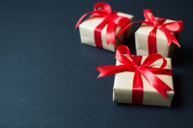 Şenlik konsepti. El işi kağıtlı hediyeler. Siyah arka planda kırmızı bir fiyonk. Yılbaşı, yeni yıl ve tatiller için kompozisyon. metin için yer alan düz uzanma.