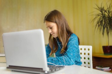 Kız, öğretmenin ödevini dizüstü bilgisayarının önüne yazar. Online eğitim. Evde eğitim