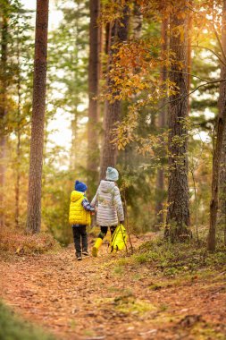 Oğlan ve bir kız, sonbahar ormanında bir patika boyunca sırt çantasıyla yürüyorlar. Çocuklar kampa gitti.