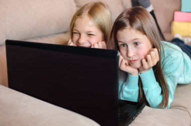 İki kız kanepede uzanıyor ve dizüstü bilgisayara bakıyor. İletişim kuruyorlar ve tatil için tebrik ediyorlar. Arkaplanda renkli hediyeler.