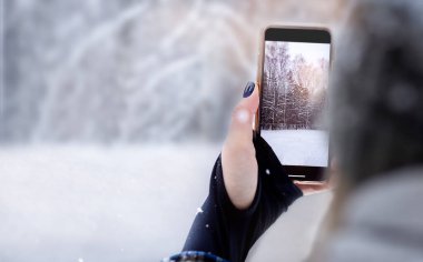 Kadın cep telefonuyla güzel bir kış ormanının fotoğraflarını çekiyor. Telefon ekranı yakın plan. Çözünürlükte önplan