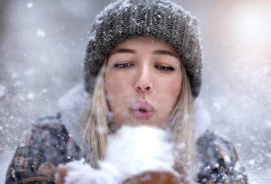 Sıcak şapkalı genç bir kadın kara üfledi. Kar doğrudan kameraya doğru uçuyor. Kış konsepti