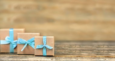 Three craft gift boxes with blue ribbons on a wooden brown background