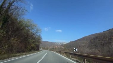 Ağaçlarla çevrili virajlı bir dağ yolunda yavaş bir araba sürüyor. Uzakta bir dağ köyü. Sonbahar, açık mavi gökyüzü
