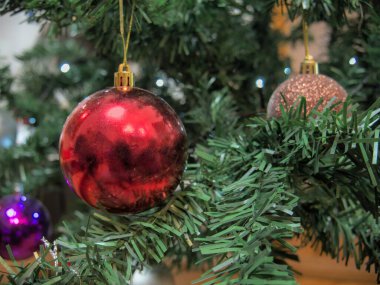Yansıtıcı bir yüzeyi olan kırmızı Noel topu, yapay bir Noel ağacının dalına asılmış.