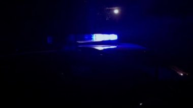 Karanlıkta güçlü bir polis arabası yanıp sönüyor. Mavi ışık fenerlerin her iki tarafında.