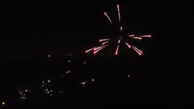 Gece geç saatlerde karanlık gökyüzüne karşı havai fişekler, tepede evler, hava manzaralı.