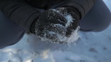 Kar topu yapan birinin eline yakın plan bir çekim. Siyah yün eldiven, siyah ceket ve mavi eşofman giyiyor.