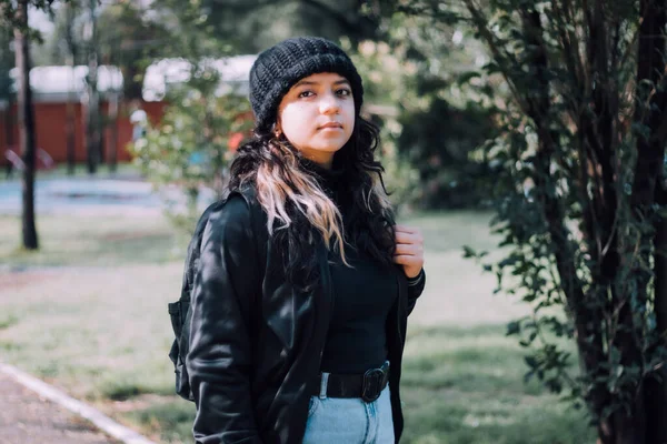 Latin üniversiteli kız parkta siyah giyinmiş duruyor.