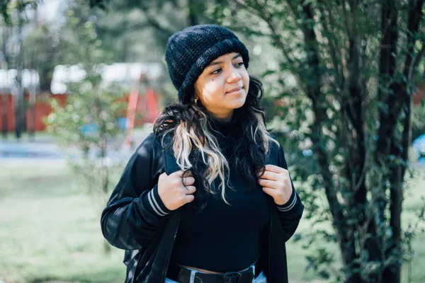 Gülümseyen Latin üniversiteli kız parkta yürüyor.