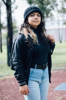 Düşünceli Latin üniversiteli kız parkta yürüyor.