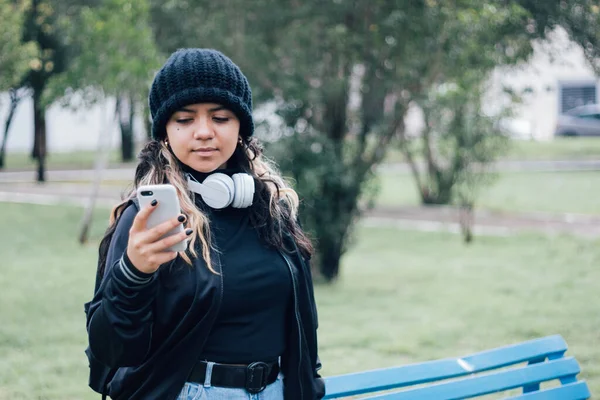 Parktaki Latin üniversiteli kız telefonuyla internette geziniyor.