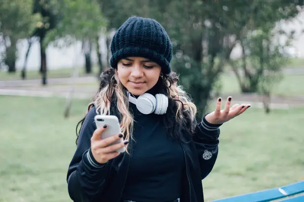 Parktaki Latin üniversiteli kız telefonuyla internette geziniyor.