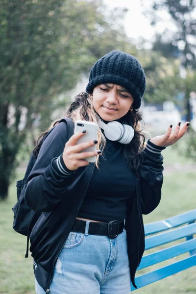 Parktaki Latin üniversiteli kız telefonuyla internette geziniyor.