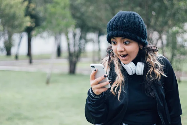 Parktaki Latin üniversiteli kız telefonuyla internette geziniyor.