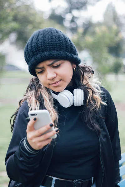 Parktaki Latin üniversiteli kız telefonuyla internette geziniyor.