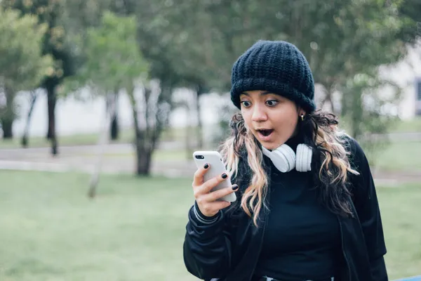 Parktaki Latin üniversiteli kız telefonuyla internette geziniyor.