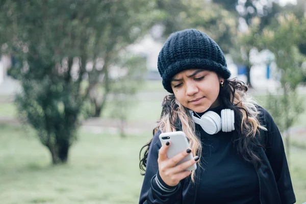 Parktaki Latin üniversiteli kız telefonuyla internette geziniyor.
