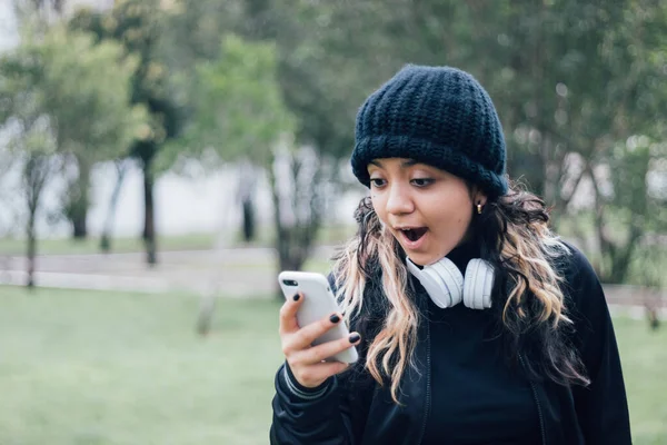 Parktaki Latin üniversiteli kız telefonuyla internette geziniyor.