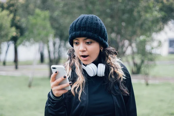 Parktaki Latin üniversiteli kız telefonuyla internette geziniyor.