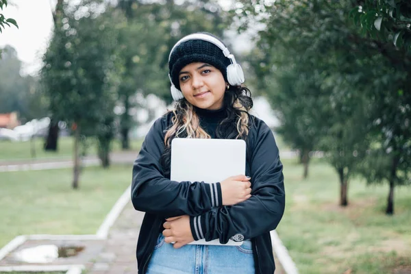 Parkta dizüstü bilgisayarla yürüyen Latin üniversiteli kız.