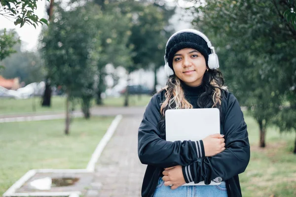 Parkta dizüstü bilgisayarla yürüyen Latin üniversiteli kız.