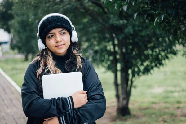 Parkta dizüstü bilgisayarla yürüyen Latin üniversiteli kız.