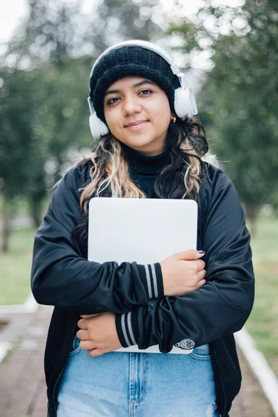 Parkta dizüstü bilgisayarla yürüyen Latin üniversiteli kız.