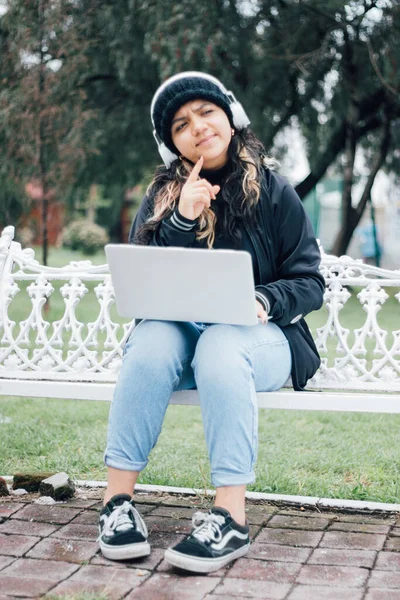 Latin üniversiteli bir kız parkta bankta oturmuş bilgisayarla düşünüyor.