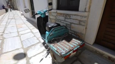 Yunan caddesinde duran üç tekerlekli motosiklet. Antik caddedeki kapının yanında bir bisiklet. Sokakta yeşil scooter (vespa).