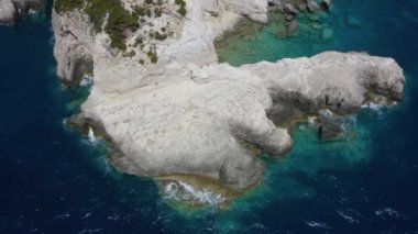 Mavi okyanustaki bir kayanın havadan çekilmiş görüntüsü. Bir deniz pelerininin etrafında yarı daire uçuş.